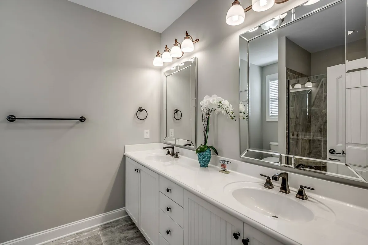 A bright, inviting bathroom with a double vanity, large mirrors, elegant fixtures, and a decorative plant. Morning sunlight enhances the fresh and clean look, making it an ideal space for winding down or starting the day.