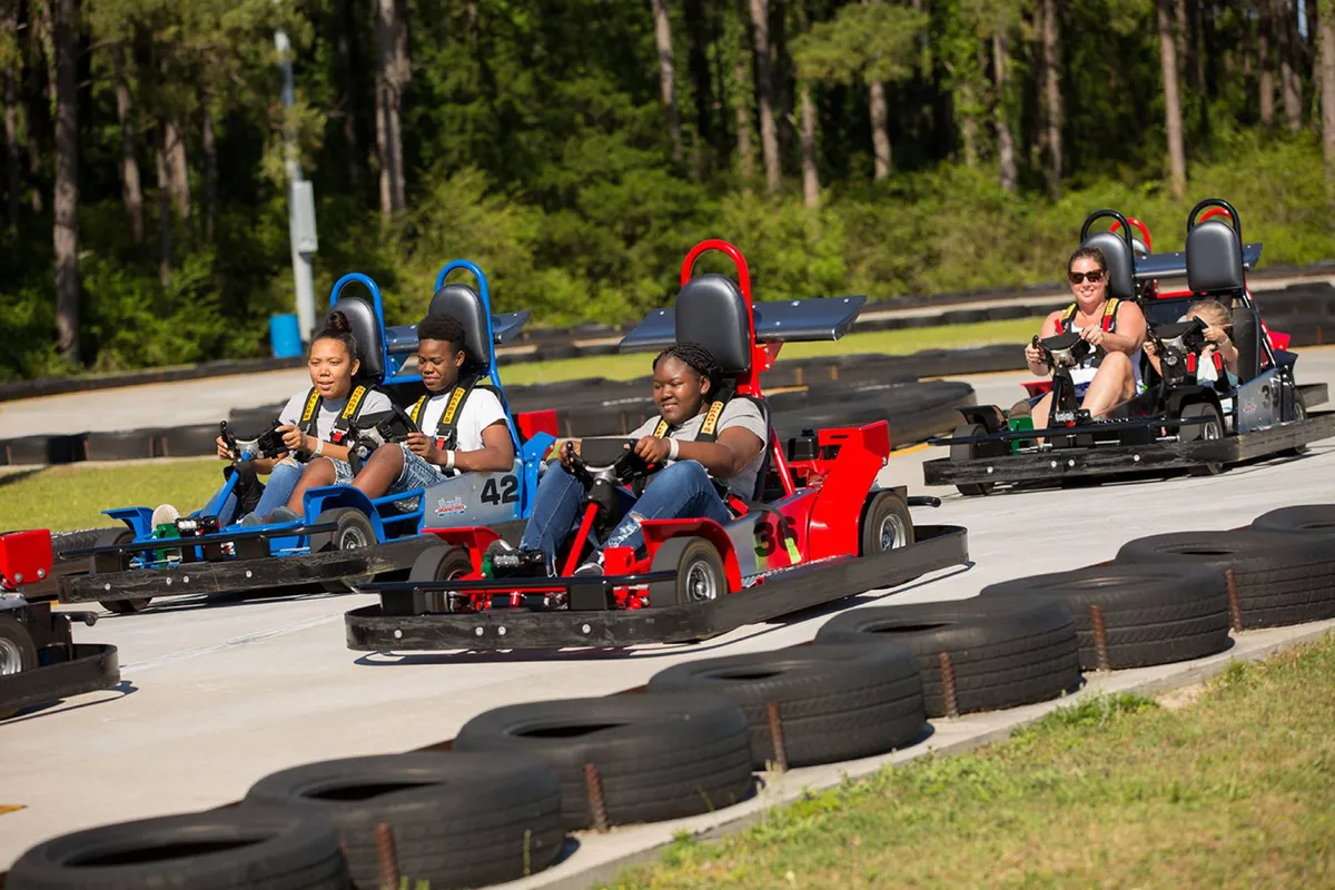 This exterior image features families racing go-karts on a lush outdoor track surrounded by greenery. Laughter and fun are evident as participants compete, creating a dynamic sense of excitement and togetherness.