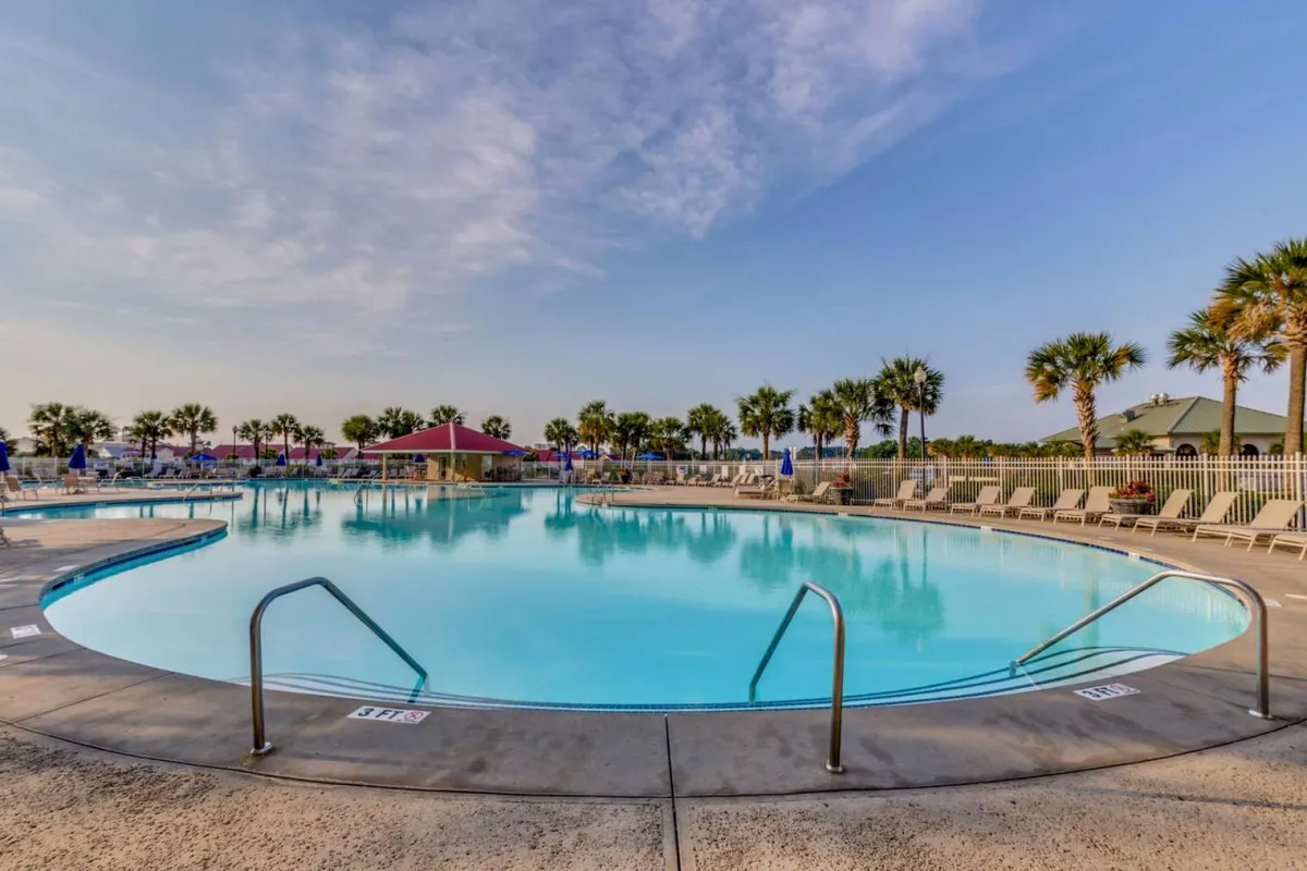 A wide, sparkling saltwater swimming pool surrounded by inviting lounge chairs and stately palm trees, with a red-roofed structure in the background. The setting suggests a luxurious resort experience, ideal for swimming, sunbathing, and socializing in the sun or at sunset.
