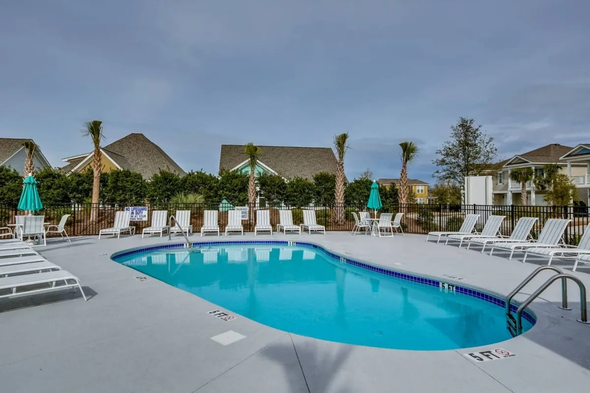 This vibrant exterior image focuses on a large resort-style saltwater swimming pool surrounded by palm trees and lounge chairs. Bright umbrellas provide shade, and the atmosphere is lively yet relaxing, perfect for families enjoying poolside activities under clear skies.