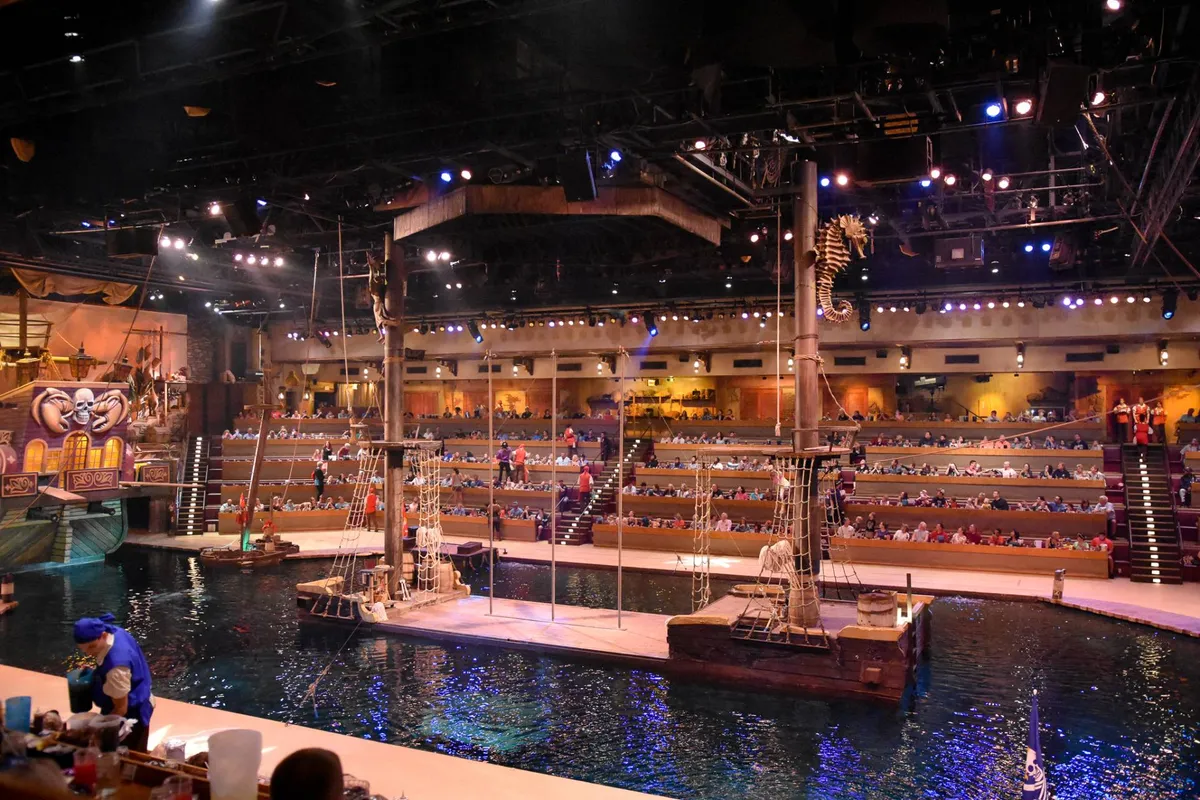 A cozy living room setup featuring a central stage, pirate ship decor, and inviting audience seating. The scene is lively yet comfortable, suggesting a space where guests can gather, relax, or unwind after a day of adventure.